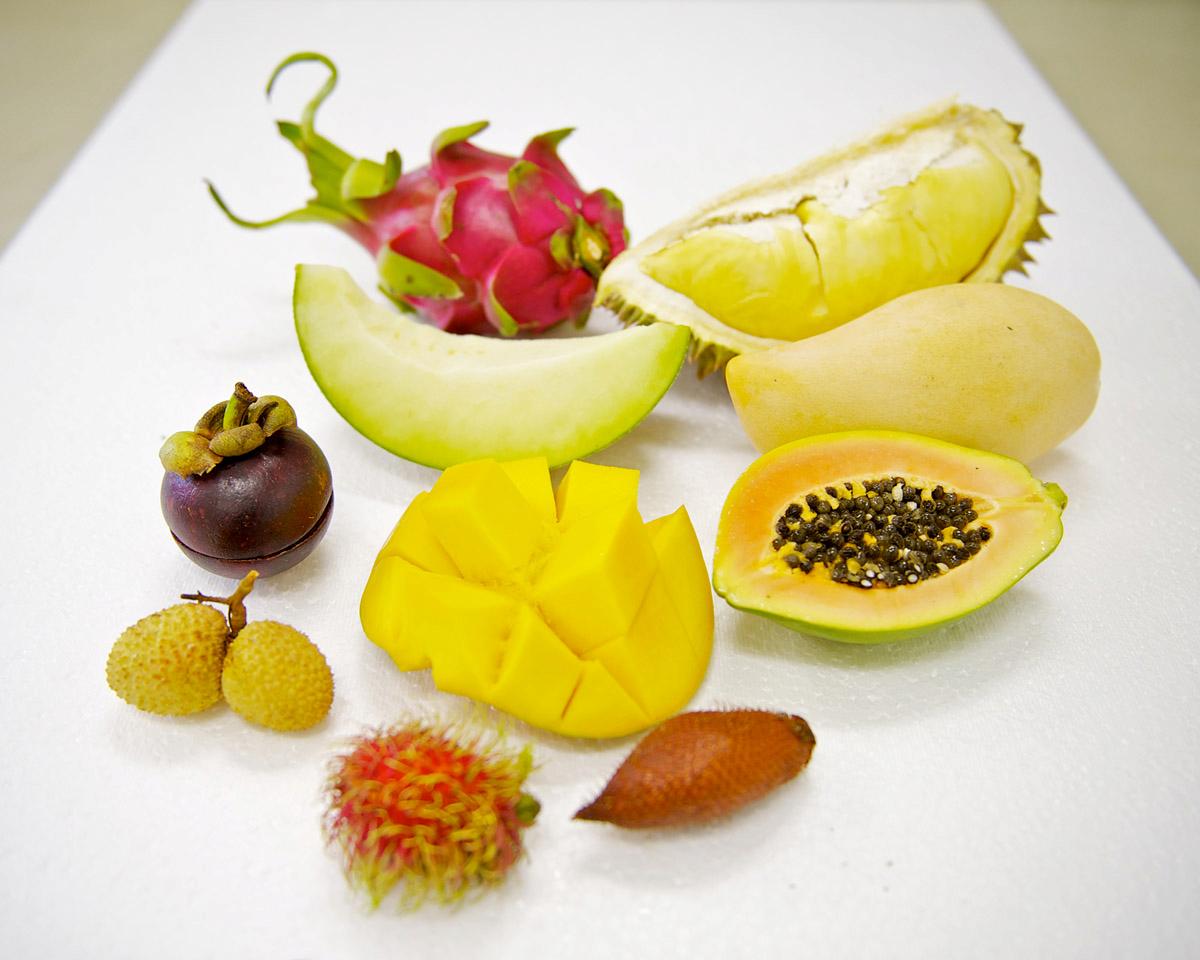 The image showcases a variety of exotic fruits, including dragon fruit, durian, mango, papaya, mangosteen, lychee, rambutan, salak, and melon. These fruits are arranged on a white surface, likely for display or presentation.