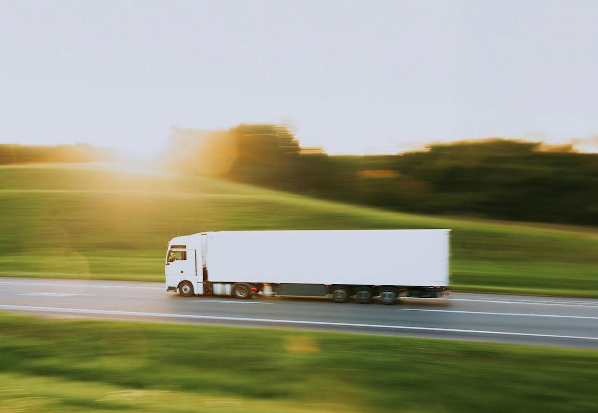 A white semi-truck is driving on a highway. The image has a motion blur effect, suggesting speed.