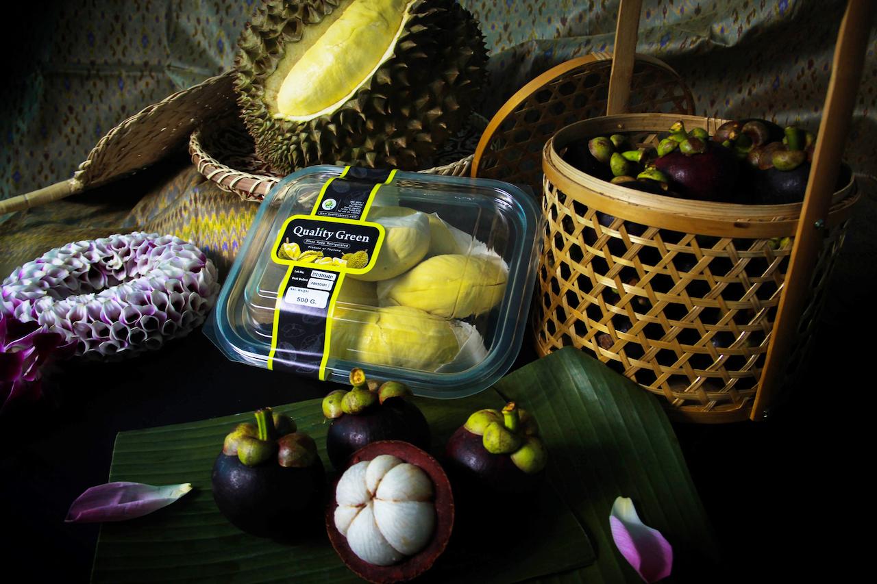 The image features a still life arrangement of tropical fruits, including durian and mangosteen, along with a flower garland. The fruits are presented in various forms, such as whole, cut, and packaged.